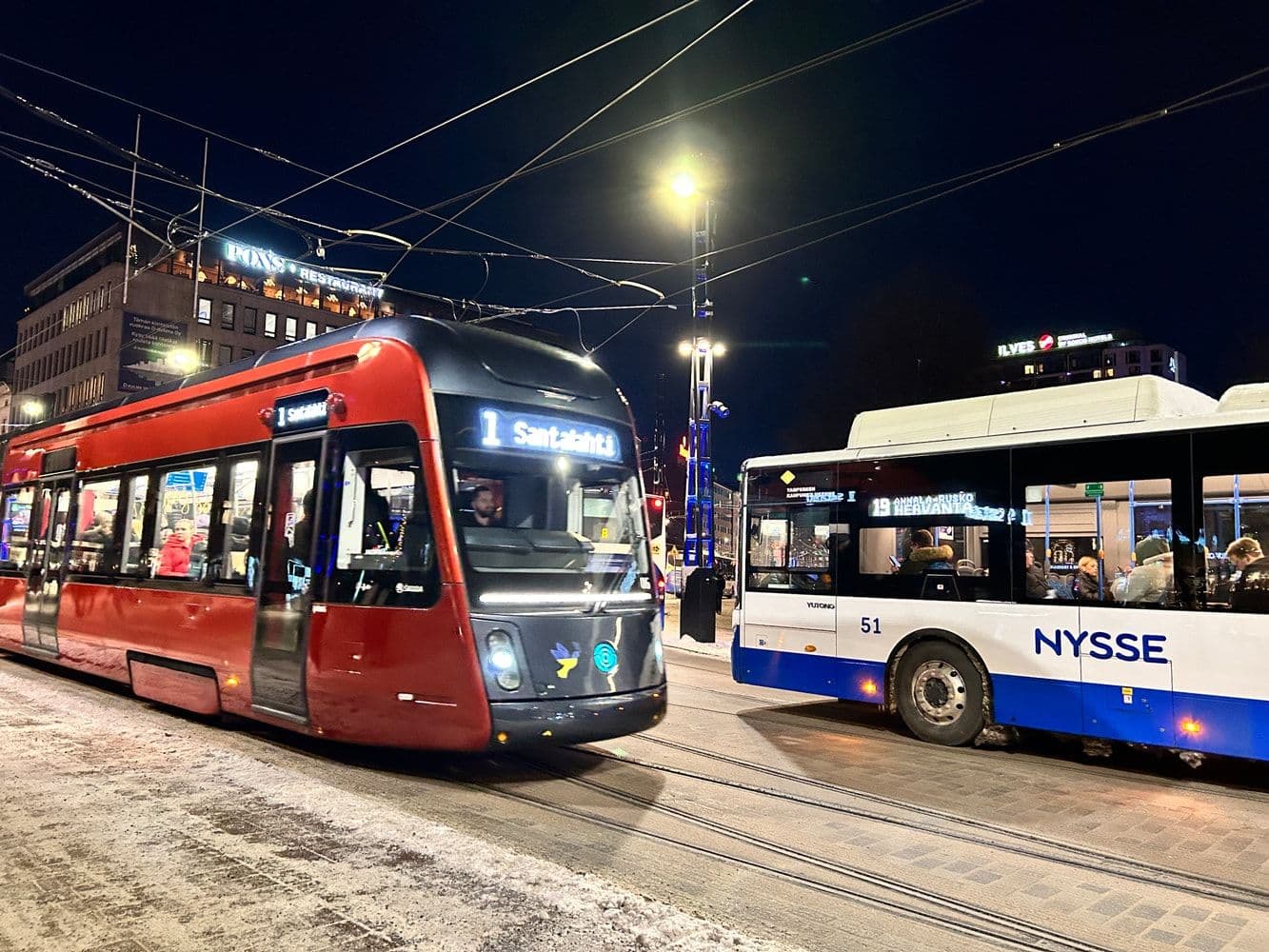 Punainen ratikka ja Nyssen bussi pysäkillä Tampereella illalla